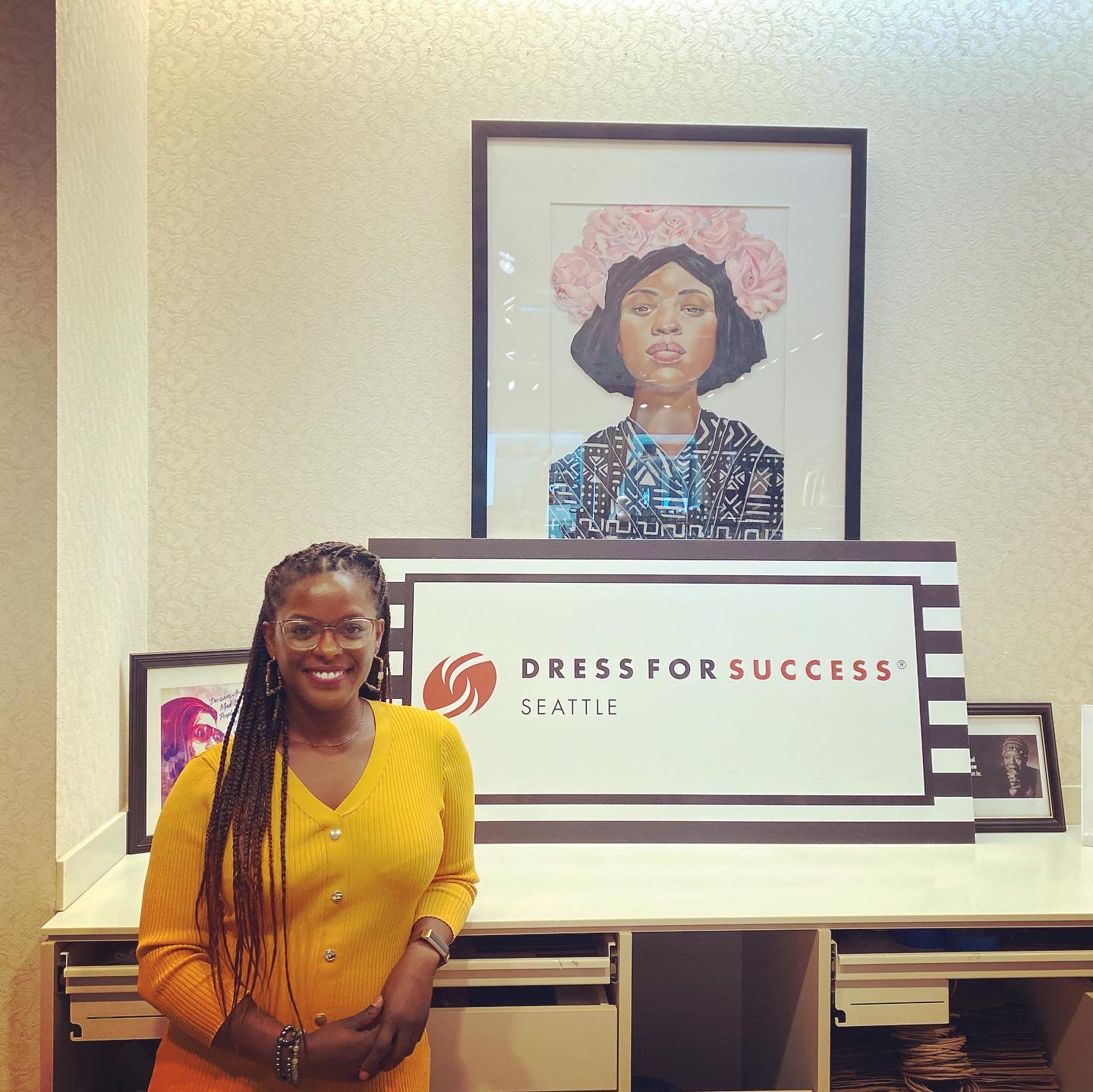 Kiesha standing next to Bonnie's Painting in the Dress for Success headquarters